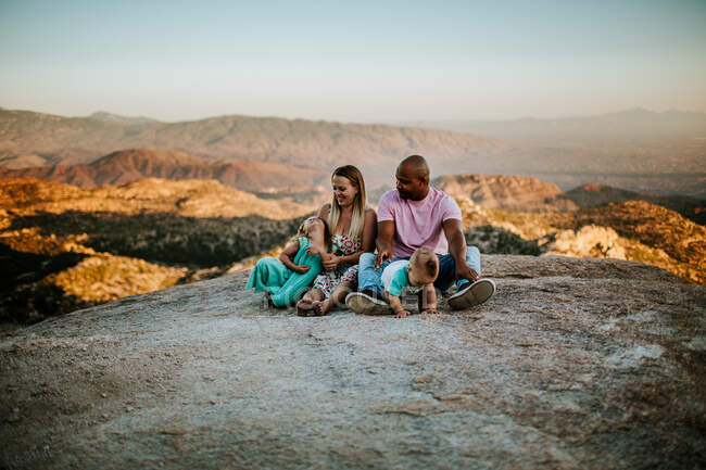 Familia de cuatro personas sentadas en una gran roca sobre una ciudad desierta - foto de stock