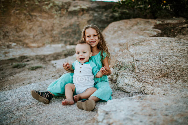 Glückliche junge Geschwister sitzen lächelnd zusammen auf einem Felsen — Stockfoto