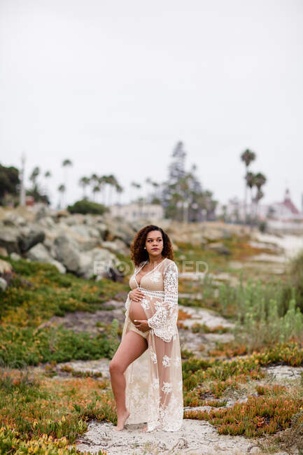 Молодая беременная женщина позирует на пляже в чистом платье — стоковое фото