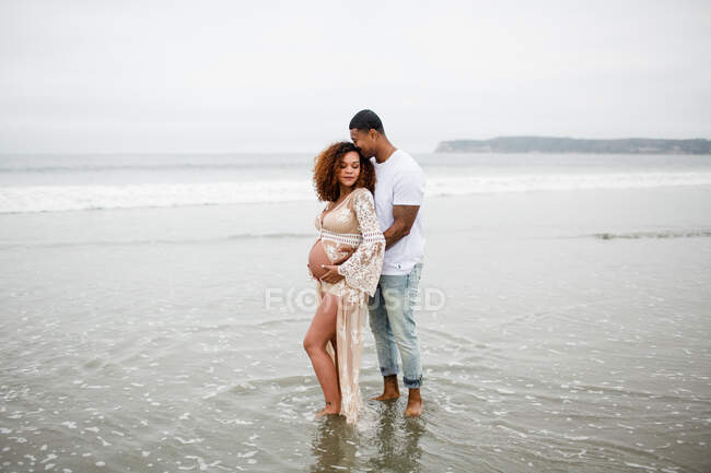 Gemischtes Paar posiert am Strand, Umstandsmode — Stockfoto