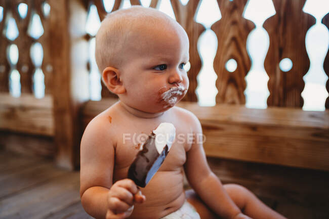 White male baby eating ice cream topless on the ground in summer — Stock Photo