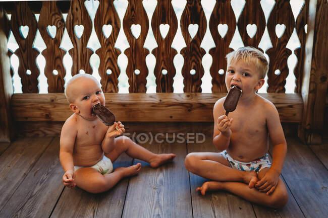 Jeunes garçons blonds mangeant de la crème glacée seins nus sur le sol en été — Photo de stock