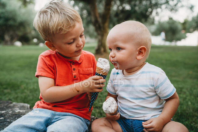 Frères blancs mâles partageant la crème glacée assis sur l'herbe — Photo de stock