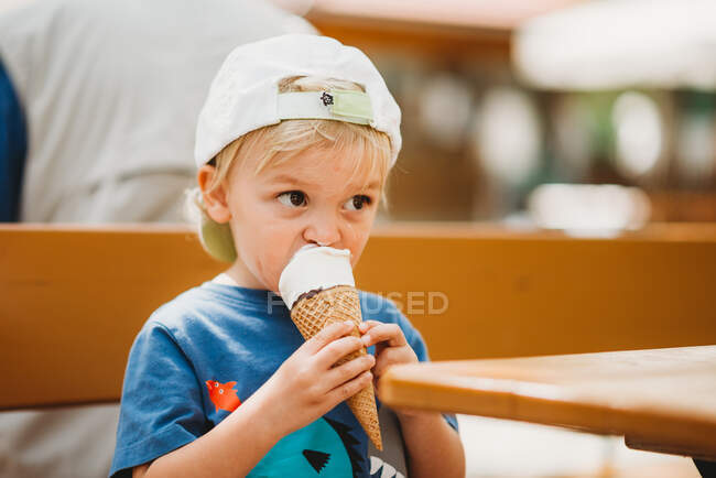 Blonde toddler eating ice cream cone sitting on bear garden bench — Stock Photo