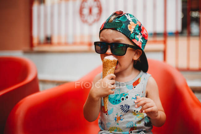 Young toddler eating ice cream cone with cap to back and sunglasses — Stock Photo