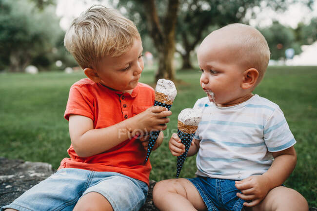 Baby and toddler sharing some ice cream looking at each other — Stock Photo