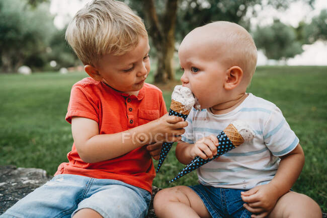 Big brother sharing his ice cream cone with his baby sibling — Stock Photo