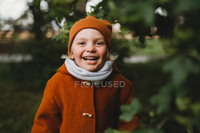 Bom menino olhando sorrindo no parque entre folhas vestindo tons de terra — Fotografia de Stock