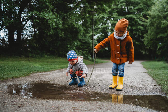 Vue de face de jeunes garçons jouant avec des bâtons dans une flaque d'eau dans le parc — Photo de stock