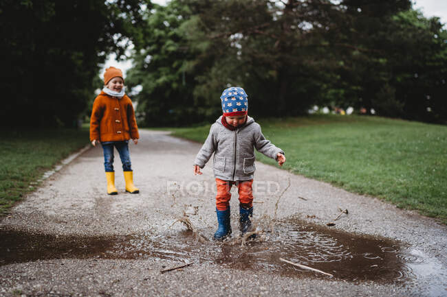 Jovens rapazes pulando nas poças no parque em dia nublado — Fotografia de Stock