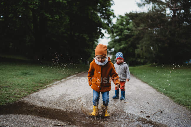 Young kids jumping in the puddles at the park on cloudy day — Stock Photo