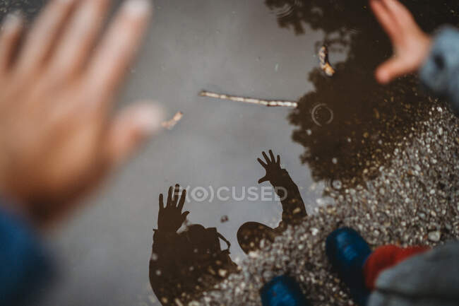 Vista desde arriba del reflejo de las manos sobre un charco de madre e hijo - foto de stock