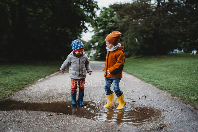 Männliche Kinder springen bei Regen in den Pfützen im Park — Stockfoto