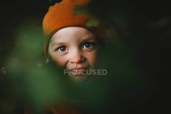 Cara de menino bonito entre folhas usando um chapéu de gorro — Fotografia de Stock