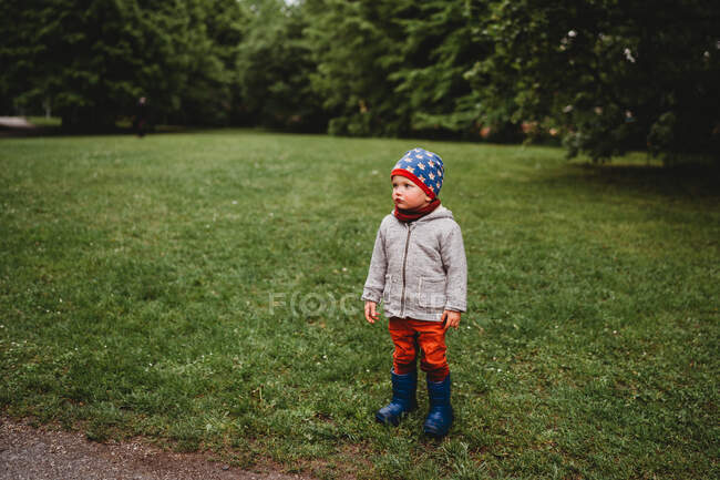 Jeune garçon avec un visage sérieux debout au parc regardant vers le côté — Photo de stock