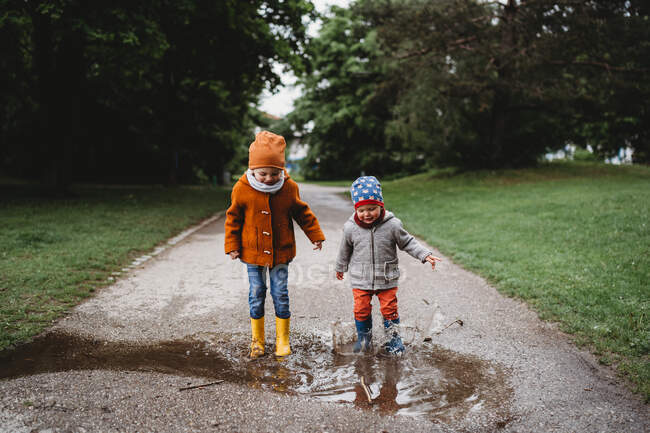 Young boys jumping in the puddles at the park on cloudy day — Stock Photo