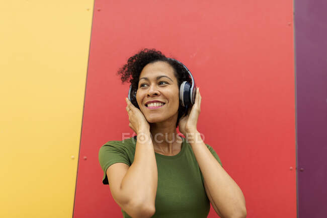 Латинська жінка, одягнена в навушники, слухає музику на фоні барвистих стін. — стокове фото