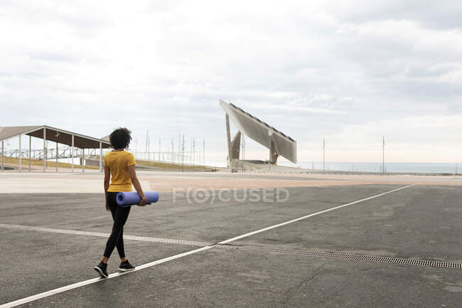 Mujer de pelo rizado caminando al aire libre con esterilla de yoga - foto de stock