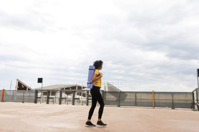 Frau läuft mit Yogamatte im Stadtpark Seitenansicht — Stockfoto