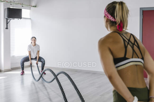 Mature woman doing battlerope exercise with personal trainer at gym — Stock Photo