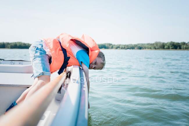 Молодий хлопчик занурює руку у воду, перебуваючи на човні влітку — стокове фото