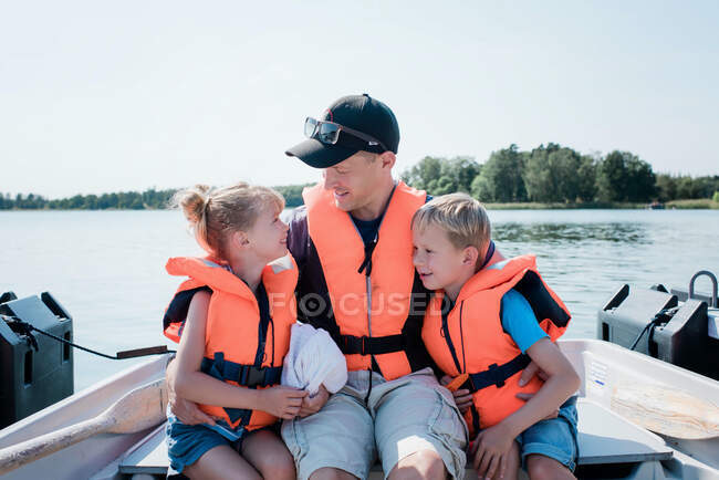 Père assis embrassant ses enfants sur un bateau à rames en été en Suède — Photo de stock