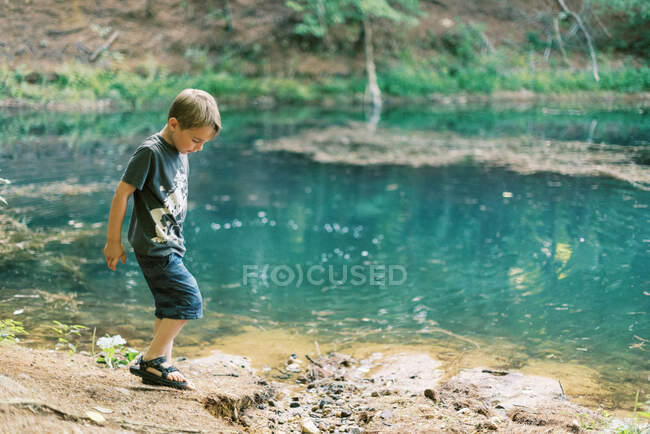 Пятилетний мальчик играет у бирюзового пруда в лесу — стоковое фото