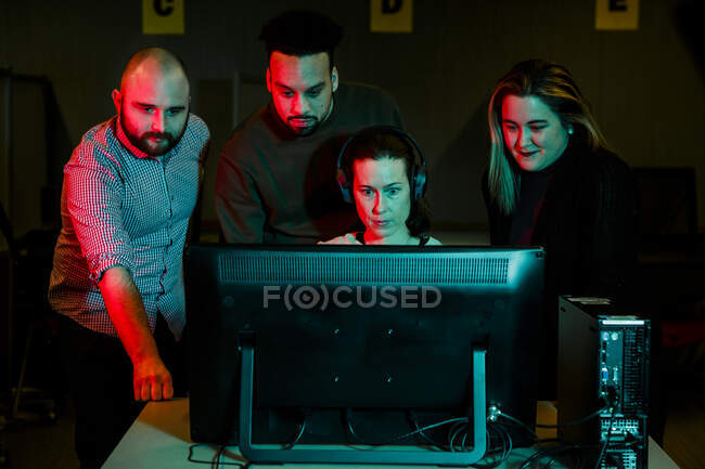 Женщина собирает команду студентов за компьютером в темной комнате — стоковое фото