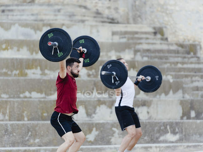 Dos levantadores de pesas levantando pesas en un entorno urbano. - foto de stock