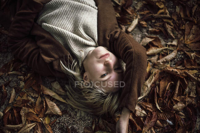 Retrato de una mujer rubia acostada en las hojas de otoño. - foto de stock
