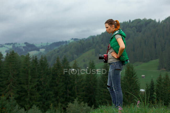 Chica fotógrafa en las montañas dispara el paisaje en el fondo de un día nublado - foto de stock