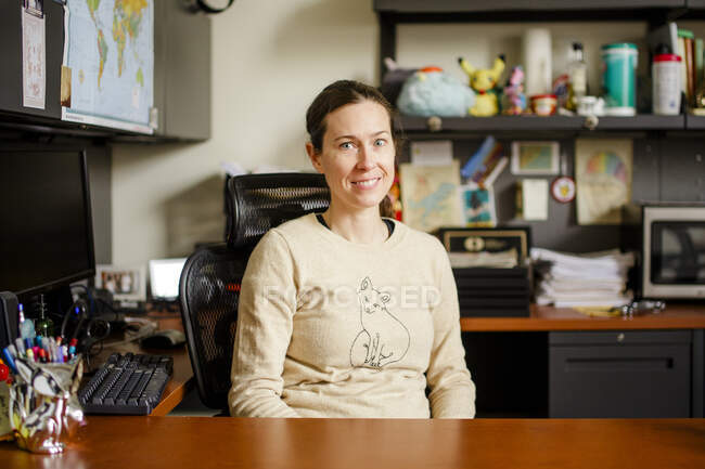 Una professoressa sorridente siede alla sua scrivania in un ufficio — Foto stock