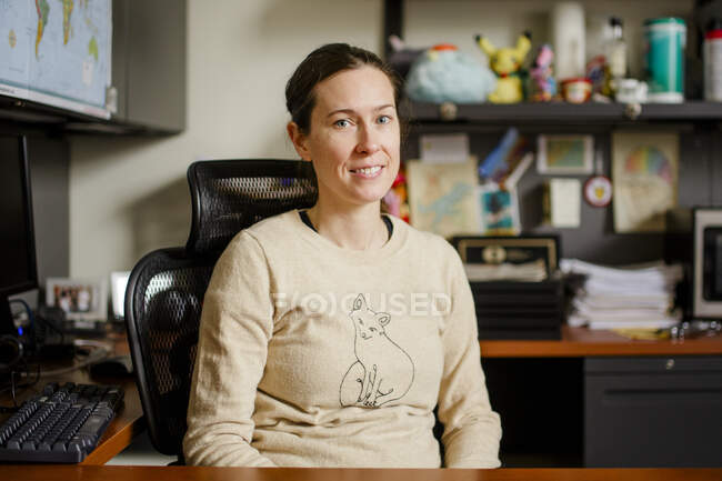 Uma mulher professora senta-se em seu escritório em uma mesa sorrindo — Fotografia de Stock