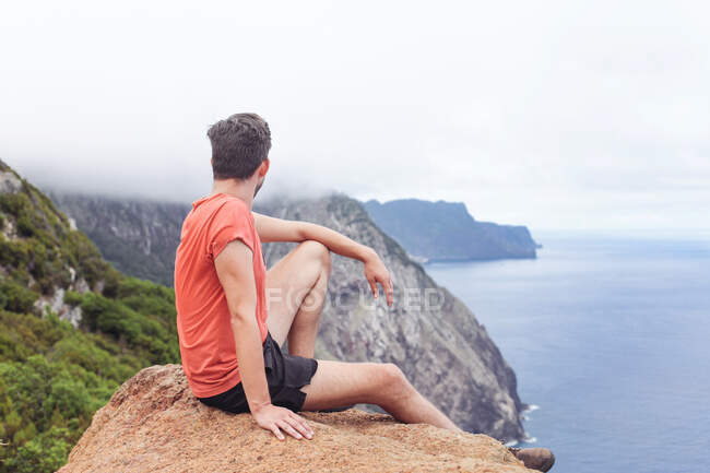 Un hombre en una roca, mirando acantilados y océanos, montañas y niebla - foto de stock