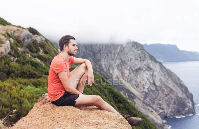 Человек на скале, смотрящий на скалы и океан, горы и туман — стоковое фото