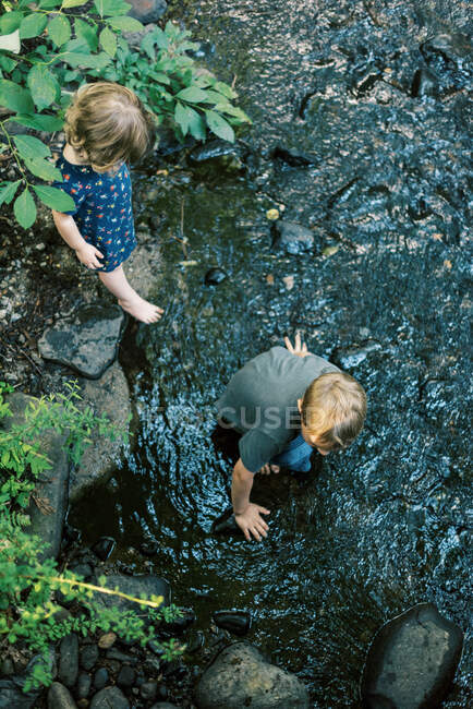 Un niño de cinco años y su hermanita buscando rocas en un río - foto de stock