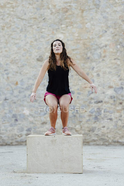 Mujer practicando crossfit saltando en una caja pliométrica. - foto de stock