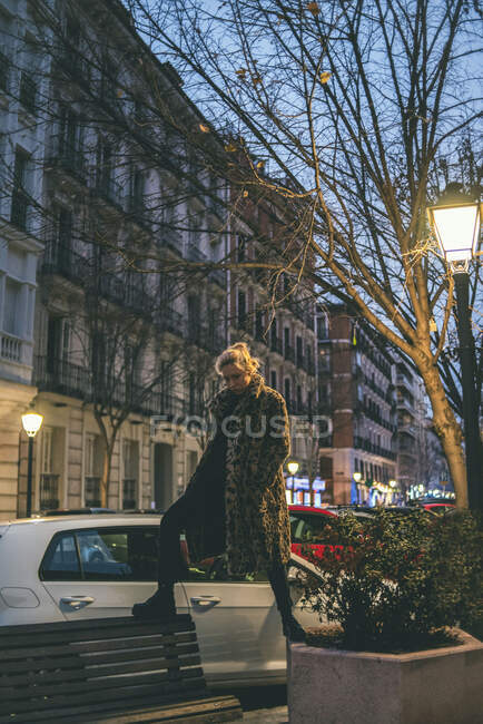 Она стоит на деревянной скамейке на городском фоне. — стоковое фото
