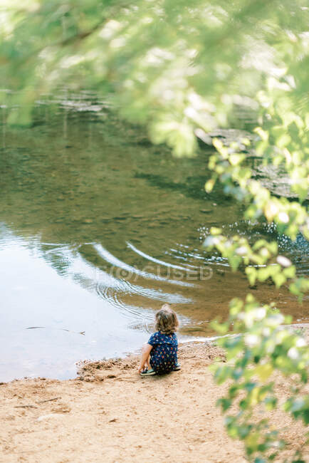 A little toddler girl sitting by a pond — Stock Photo