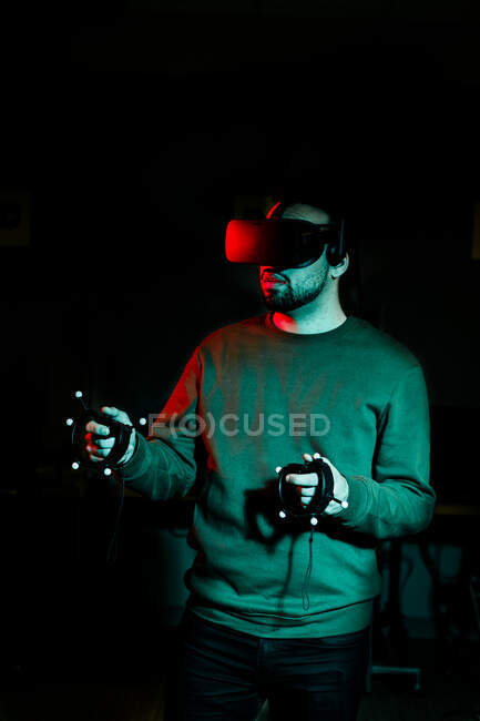 Um jovem vestindo óculos de realidade virtual fica em uma sala escura — Fotografia de Stock