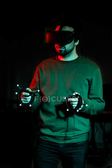 Молодой человек играет с оборудованием виртуальной реальности в темной комнате — стоковое фото