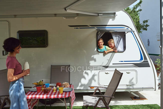 Um rapaz e uma rapariga olham pela janela de uma caravana num acampamento. Eles estão de férias.. — Fotografia de Stock