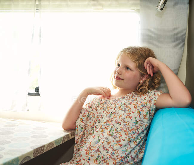 Una ragazzina in una roulotte. Lei è santa guardando fuori dalla finestra. — Foto stock