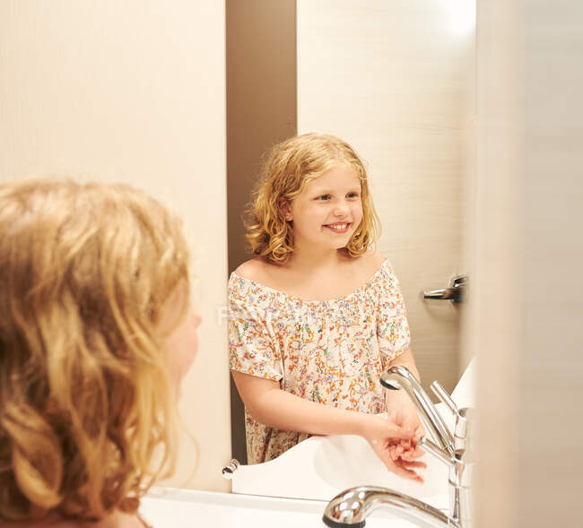Little girl washes her hands in a caravan. She is looking in a mirror. — Stock Photo