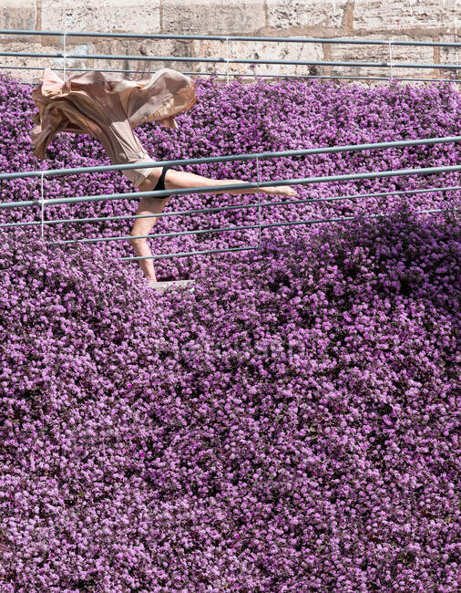 Mulher dançando cercada por flores roxas com um vestido voador — Fotografia de Stock
