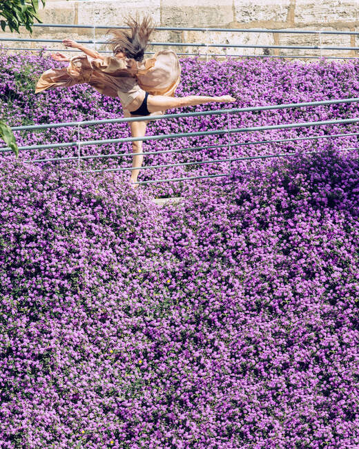 Женщина танцует в окружении фиолетовых цветов с летающим платьем — стоковое фото