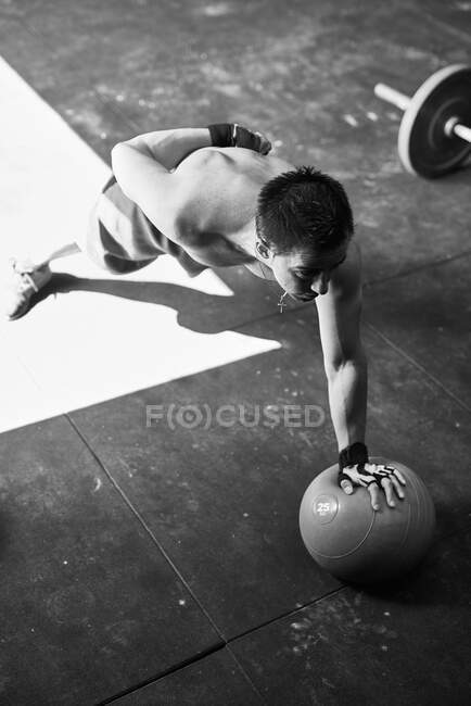 Hemdlos fitter junger Mann, der eine Hand Liegestütze mit einem schweren Ball macht — Stockfoto