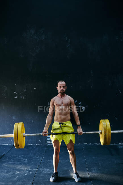 Hombre musculoso con barra sobre un fondo negro - foto de stock