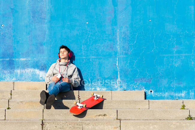 Teenager mit Kopfhörern hört Musik, während er im Treppenhaus sitzt. — Stockfoto