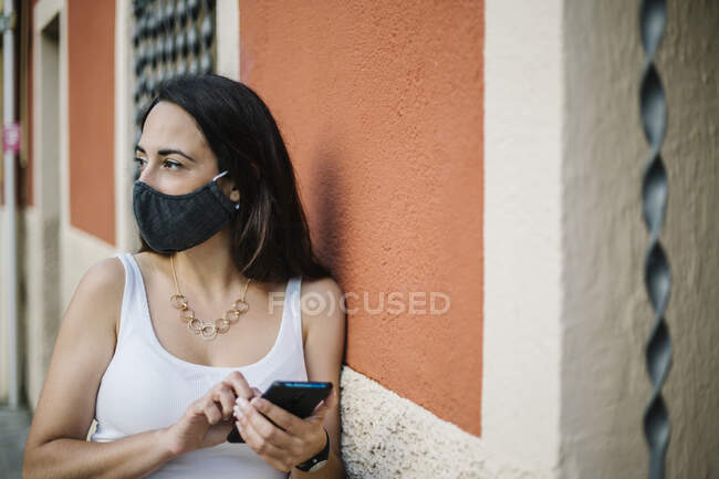 Mulher pensativa usando máscara facial usando um telefone celular na rua — Fotografia de Stock